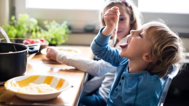 
		Two children are sitting at the dining table eating pasta without sauce.
	